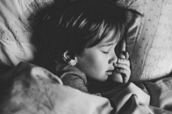 A black and white photo of a child sleeping in their bed.