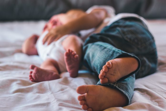 An older child lays beside a newborn.