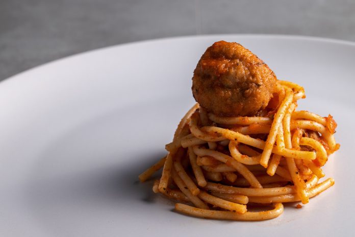 A small twirl of spaghetti with a meatball on top.