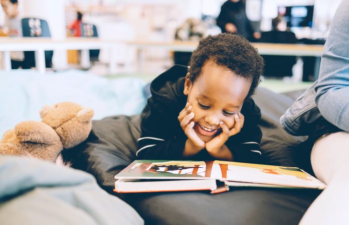 A little boy is smiling as he reads a board book..