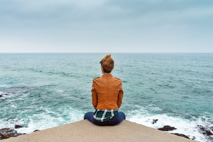 A woman sitting in front of an ocean's surf.