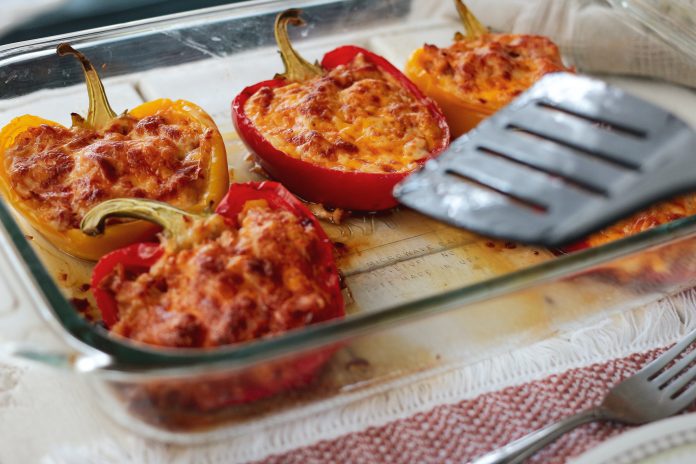 A glass casserole dish with five stuffed bell peppers and a spatula.